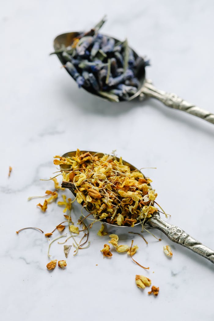 Two teaspoons filled with dried herbal flowers on a light background, showcasing a minimal still life.